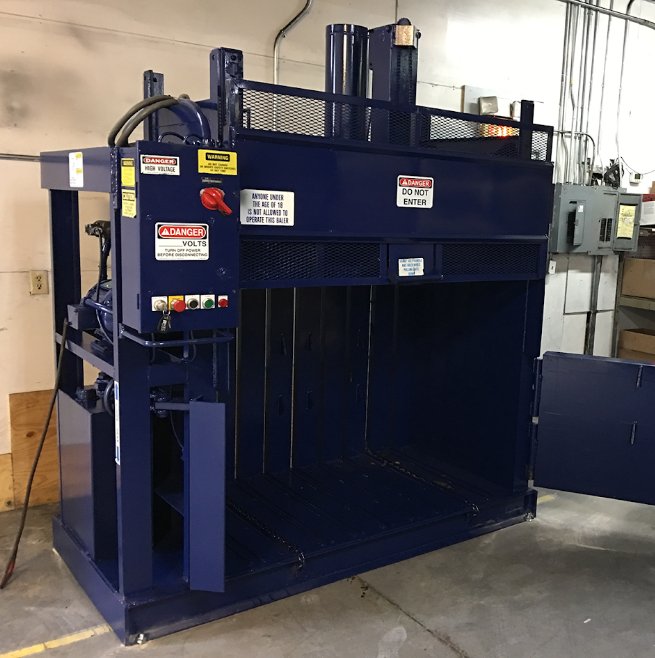 A large navy blue vertical baler sits alone in a large commercial warehouse space. It's isolated in the area.